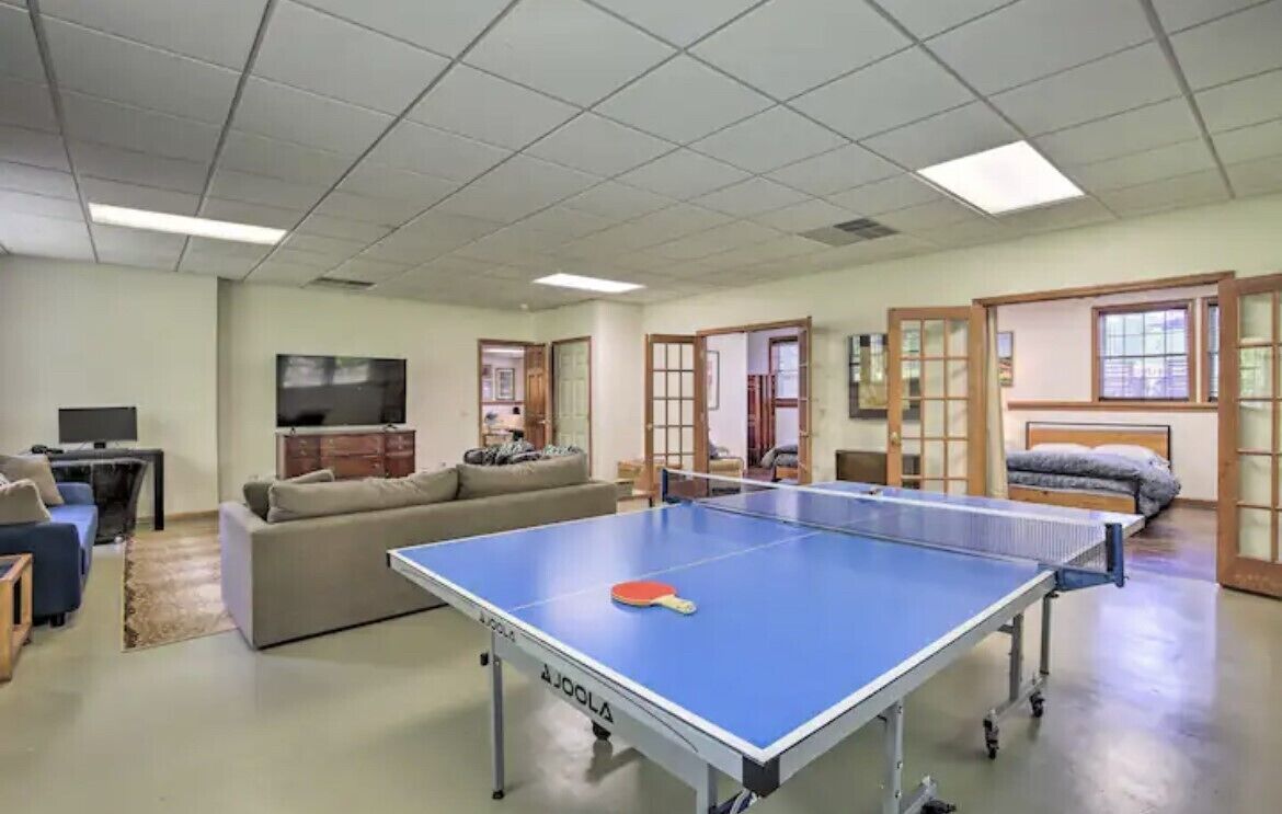 Et værelse med et ping-pong bord, en sofa, et fjernsyn og en seng med et vindue.