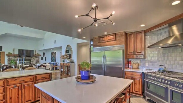 A modern kitchen with wooden cabinets, a large island, stainless steel appliances, and a unique ceiling light fixture. - Wildflower Lotus Farm a Luxurious 5bd Home w/ Pool, Firepit and more (Gardiner)