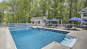 A rectangular swimming pool with a white deck, surrounded by a white fence and trees. - Wildflower Lotus Farm a Luxurious 5bd Home w/ Pool, Firepit and more (Gardiner)