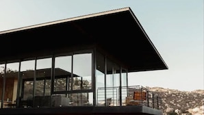 Un edificio moderno con amplios ventanales, un balcón y vistas a un paisaje rocoso.