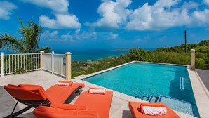 Un espace aménagé au bord de la piscine, avec des chaises longues et une vue sur l’océan.
