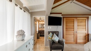 Une pièce spacieuse dotée d’une grande armoire, d’un téléviseur fixé au mur et d’un coin salon confortable avec un fauteuil et des coussins.