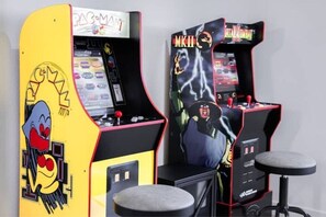 Duas máquinas de jogos eletrônicos, uma com Pac-Man e outra com Mortal Kombat, em frente a uma parede lisa.