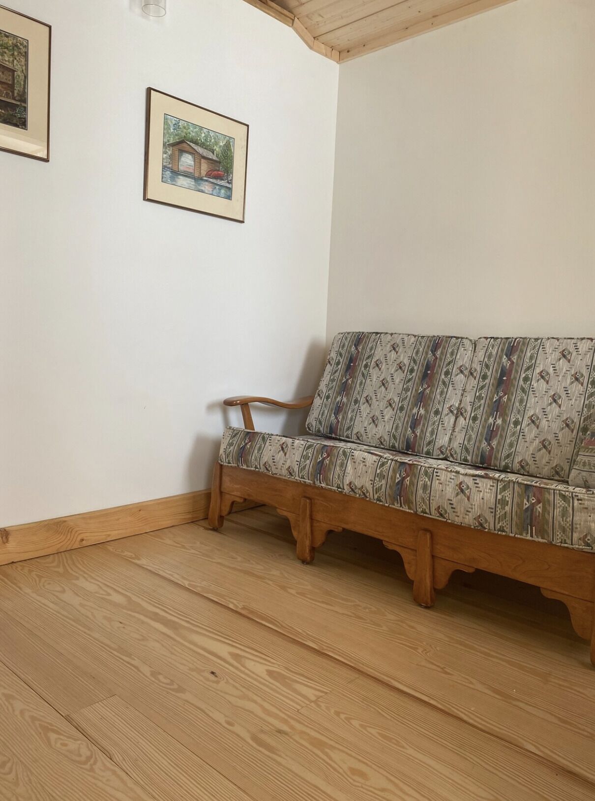 Una camera d'angolo con una panca di legno, un divano decorato e due quadri appesi al muro.