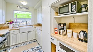 Une cuisine avec des meubles blancs, un four à micro-ondes, une machine à café et une fenêtre donnant sur un paysage verdoyant.