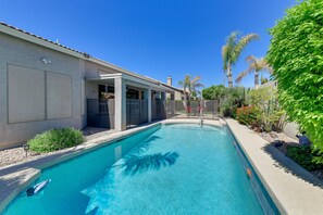 A swimming pool with a clear blue water, surrounded by a landscaped garden with various plants and a palm tree.