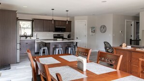 A modern kitchen with dark wood cabinets, a central island, and a dining area with a wooden table and chairs. - House near Trout Run Trail w/EV charger (Decorah)