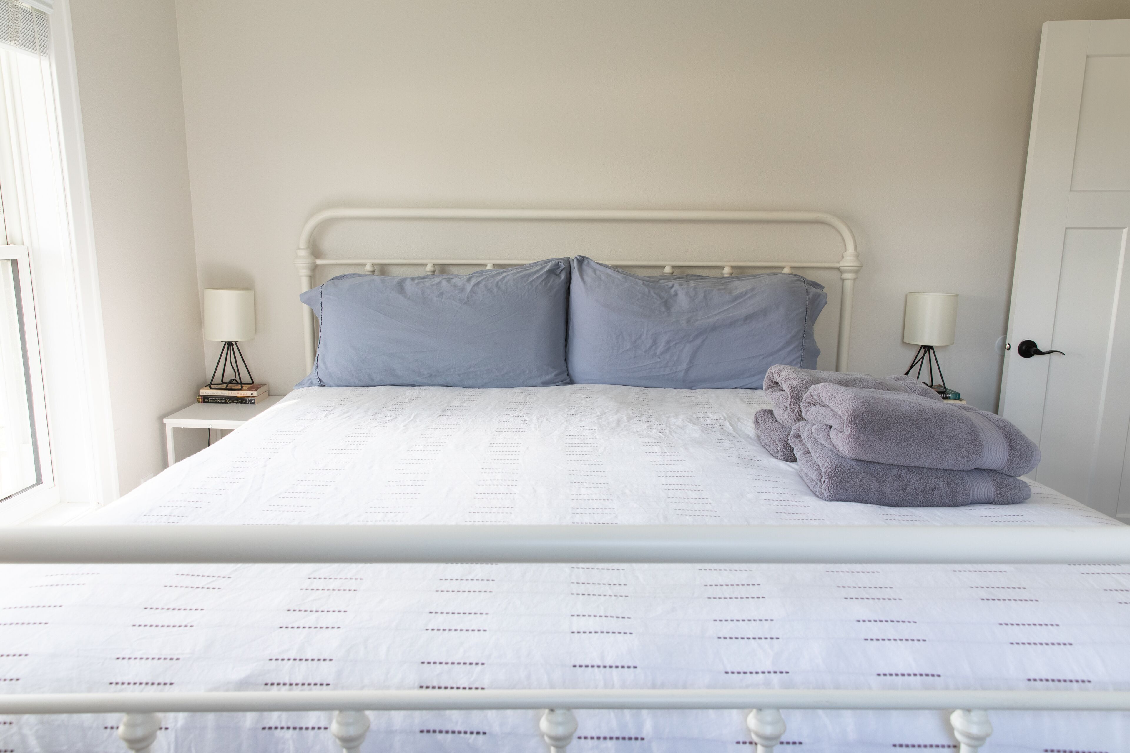 A neatly made bed with a white and patterned bedspread, two pillows, and a stack of folded towels.