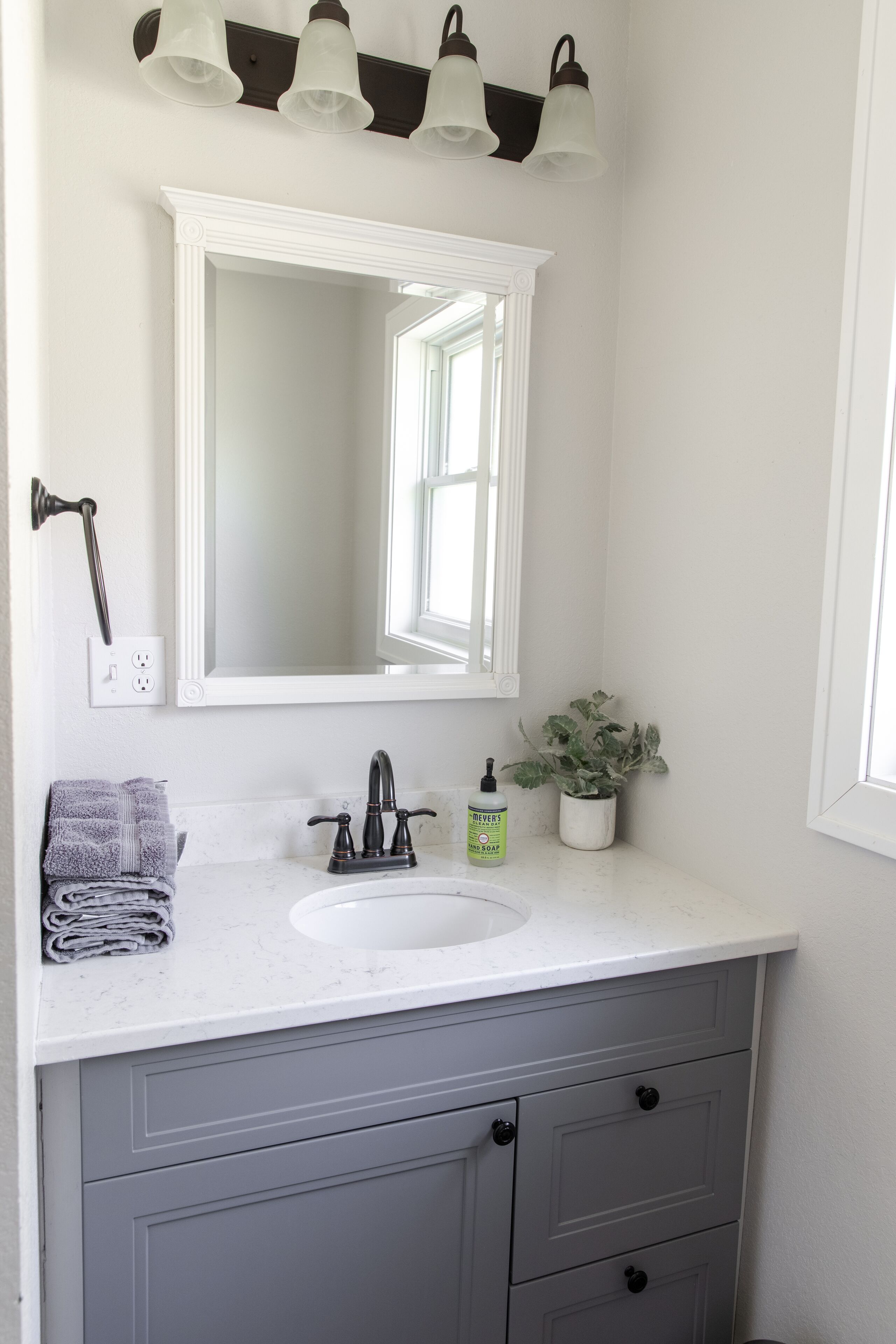 Une salle de bain avec un lavabo blanc, un miroir, une plante en pot et un porte-serviettes.