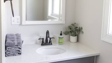 Une salle de bain avec un lavabo blanc, un miroir, une plante en pot et un porte-serviettes.