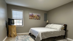 A bedroom with a bed, a TV on a wooden stand, a painting, and a lamp. - Cozy country retreat!- Close to River Run and Lake Jacksonville (Jacksonville)