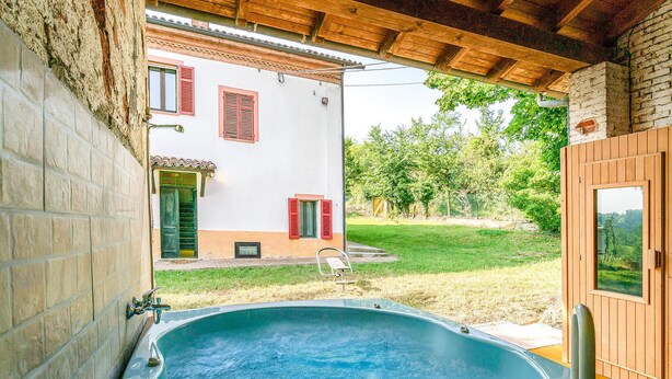 A hot tub in a covered outdoor area with a view of a white building with red shutters and a wooden door. - Pet friendly apartment (Vignale Monferrato)