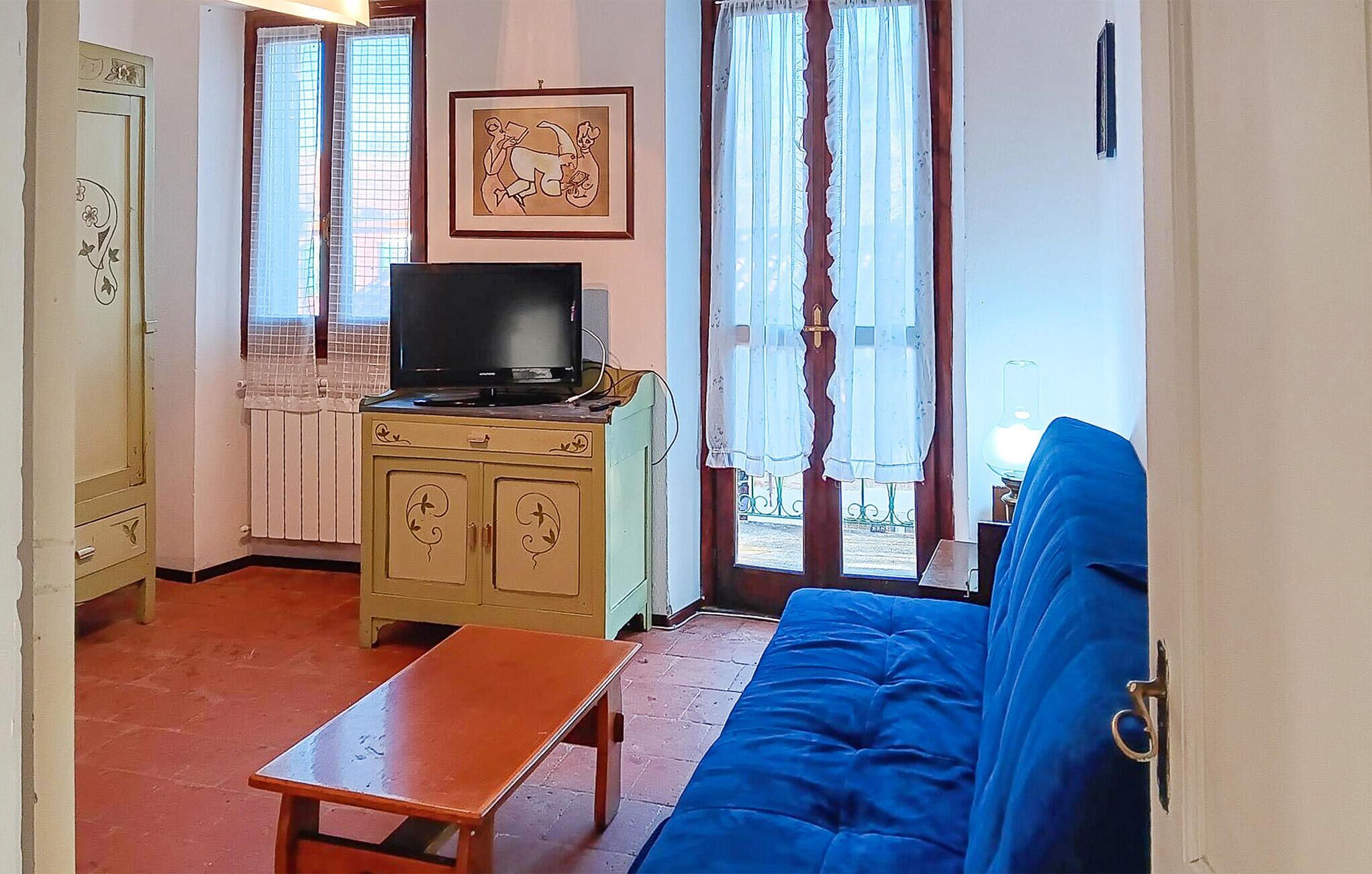 Una sala de estar con televisor sobre un mueble bajo, un sofá azul, una mesita y una ventana con cortinas.