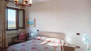 A bedroom with a bed, a chair, a nightstand, a bedside table, a lamp, a fan, a window with curtains, and a wall-mounted picture. - Pet friendly apartment (Vignale Monferrato)
