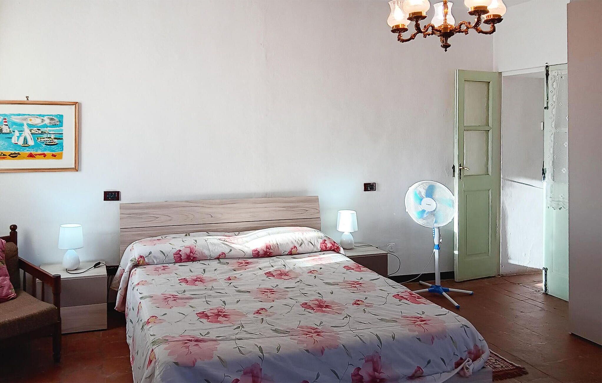 Une chambre à coucher avec un lit en bois, deux lampes de chevet, un ventilateur et une porte verte.