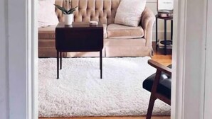 A living room with a beige sofa, a white fluffy rug, a dark wooden coffee table, and a chandelier. - Magnolia Inn - Columbia's Sweet Southern Charmer! (Columbia)