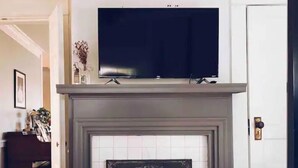 A room with a fireplace, a television mounted above it, and a door to the right. - Magnolia Inn - Columbia's Sweet Southern Charmer! (Columbia)