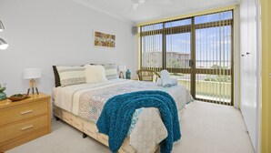 Un dormitorio con cama, mesita de noche, silla, ventana con persianas y ventilador de techo.