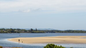 Una playa con una persona caminando por la orilla, un puente al fondo y un cielo despejado.