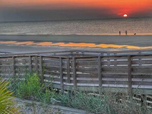 Une promenade en bois menant à une plage, avec un coucher de soleil en arrière-plan.