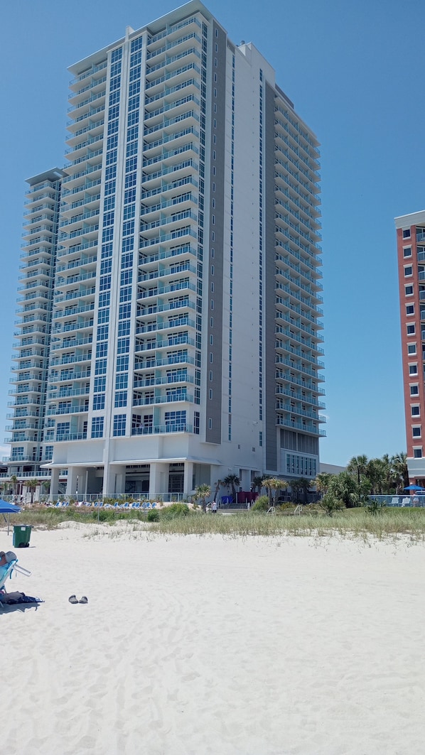 Un hotel de gran altura con varios balcones, situado junto a una playa de arena.
