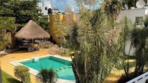 A pool area with a thatched roof structure, surrounded by greenery and a white fence. - Casa Mar y Amor / pool and interior garden18 PXS (Cancún)