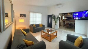 A modern living room with a sofa set, a coffee table, a TV, and a kitchen area visible through an open door. - Casa Mar y Amor / pool and interior garden18 PXS (Cancún)