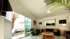 A modern living room with a large sliding glass door leading to an outdoor area, a black sofa, a wooden coffee table, and a large mirror on the wall. - Casa Mar y Amor / pool and interior garden18 PXS (Cancún)