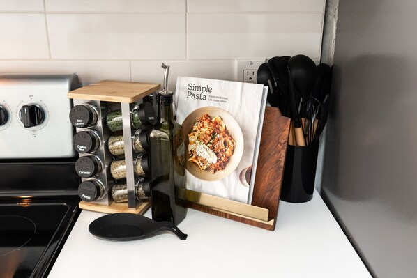 Un piano di lavoro in cucina con un libro di ricette di pasta, una spezieria e utensili da cucina.