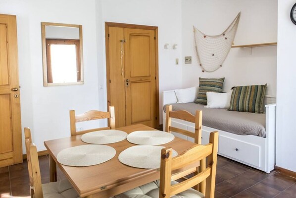 Ein Zimmer mit Holztisch, Stühlen, einem Bett mit Kissen, einer Hängematte und einem Spiegel an der Wand.