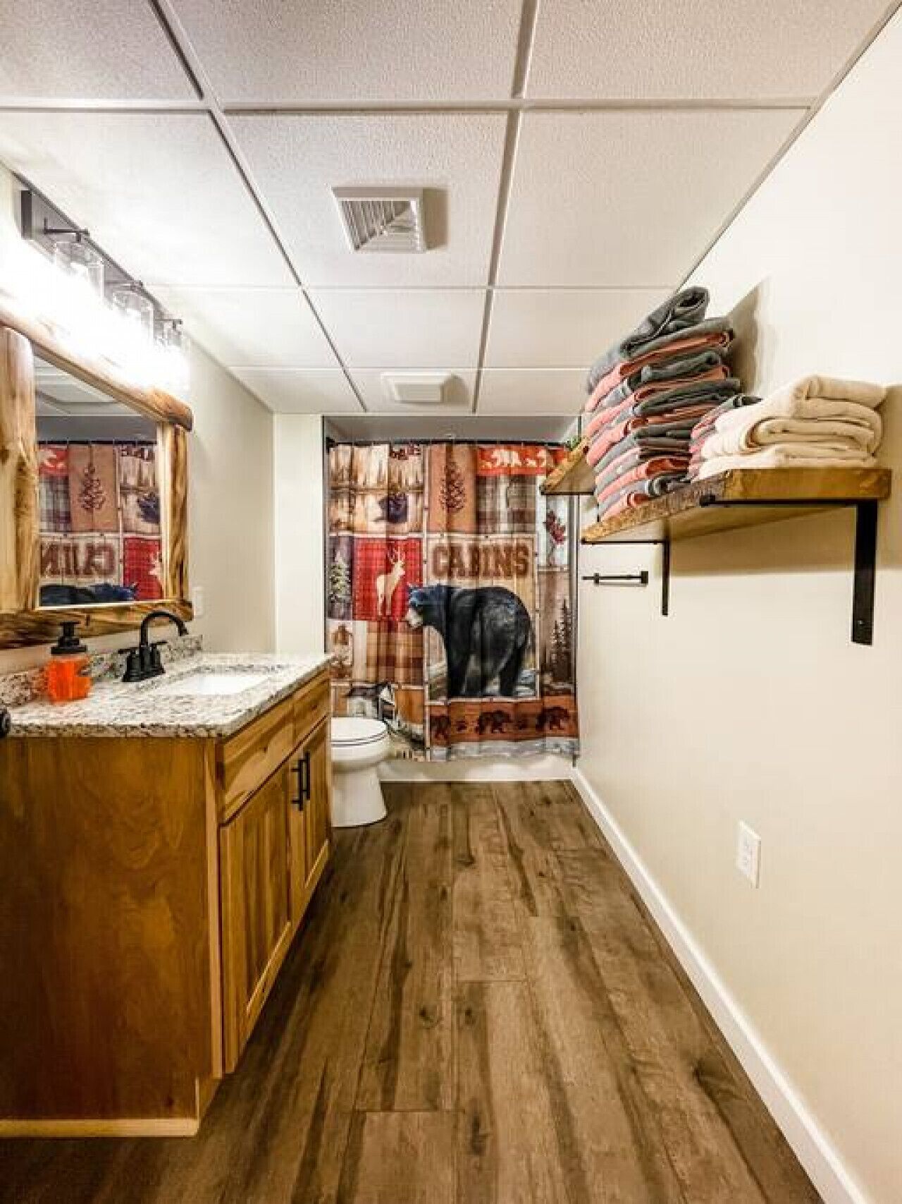 A narrow bathroom with a wooden vanity, a toilet, and a shower curtain with a bear design.