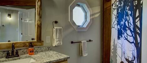 A bathroom with a wooden vanity, a large mirror, a window, and a deer painting on the wall.
