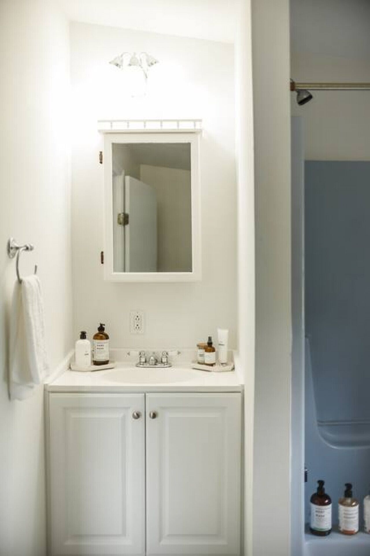 A white bathroom with a mirror above a sink, two bottles of shampoo, and a towel hanging on the wall.