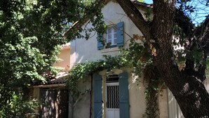 Une maison à la façade blanche, aux volets bleus et à l’entrée fermée par un portail.