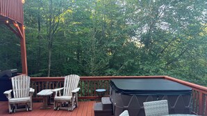 Een houten terras met Adirondack-stoelen, een ronde tafel en een jacuzzi.