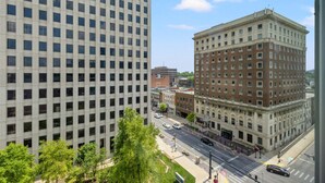 A cityscape with a tall modern building and a historic brick building with a corner entrance.