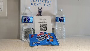 A table with two bottles of Pure Life water, a sign for Lexington, Kentucky, and a packet of Mini Chips Away cookies. - 175 LEX - Two Bedroom Condo, Walkable Downtown! (Lexington)