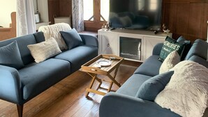 En hyggelig stue med blå sofa, et træbord og et fjernsyn på et skab.