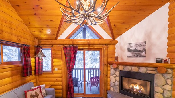A log cabin interior with a stone fireplace, wooden ceiling, and a cozy seating area. - Baker Creek | Superior Jacuzzi Suite (Lake Louise)