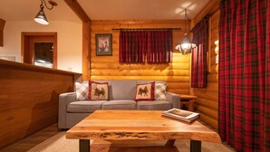 A cozy log cabin interior with a sofa, a wooden coffee table, and plaid curtains. - Baker Creek | Superior Jacuzzi Suite (Lake Louise)