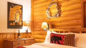 Une chambre chaleureuse aménagée dans un chalet en rondins, avec un lit, une commode en bois, un miroir et une lampe fixée au mur.