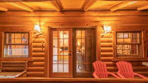 Interior de una cabaña de troncos con paredes de madera, un vidrio y dos sillas Adirondack rojas.