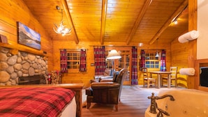 Interior acogedor de una cabaña de troncos, con chimenea, una cama grande, un sillón de cuero, una zona de comedor y un baño con bañera.