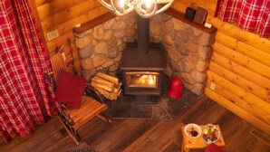 A cozy cabin interior with a stone fireplace, plaid curtains, a wooden chair, and a small table with food.