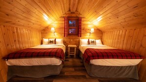 A cozy cabin room with two beds, a small table, and a window with curtains.