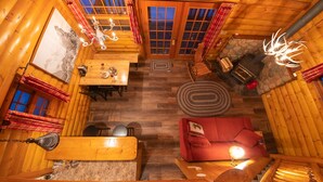 A cozy log cabin interior with a dining area, a fireplace, and a red sofa.