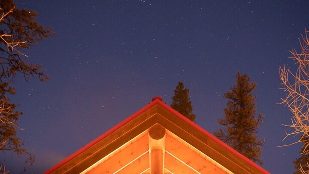 A wooden lodge with a prominent red roof, large windows, and a welcoming porch.