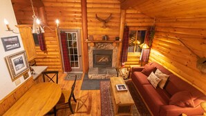 Interior acogedor de una cabaña de troncos con chimenea de piedra, muebles de madera y un sofá rojo.
