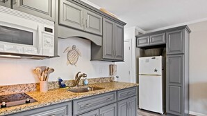 Una cocina con gabinetes grises, encimera de granito, microondas blanco y refrigerador.