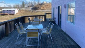 Une terrasse en bois avec une table et des chaises, une rambarde et un bâtiment doté de fenêtres.